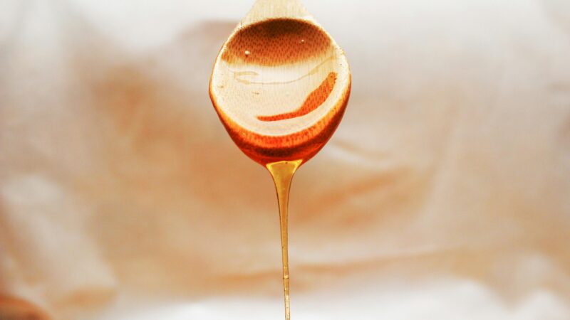 Honey drips from a wooden spoon in a warm and inviting still life setup.